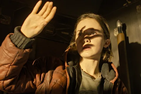 Rain Carradine raises a hand in a brown jacket aboard the Corbelan IV