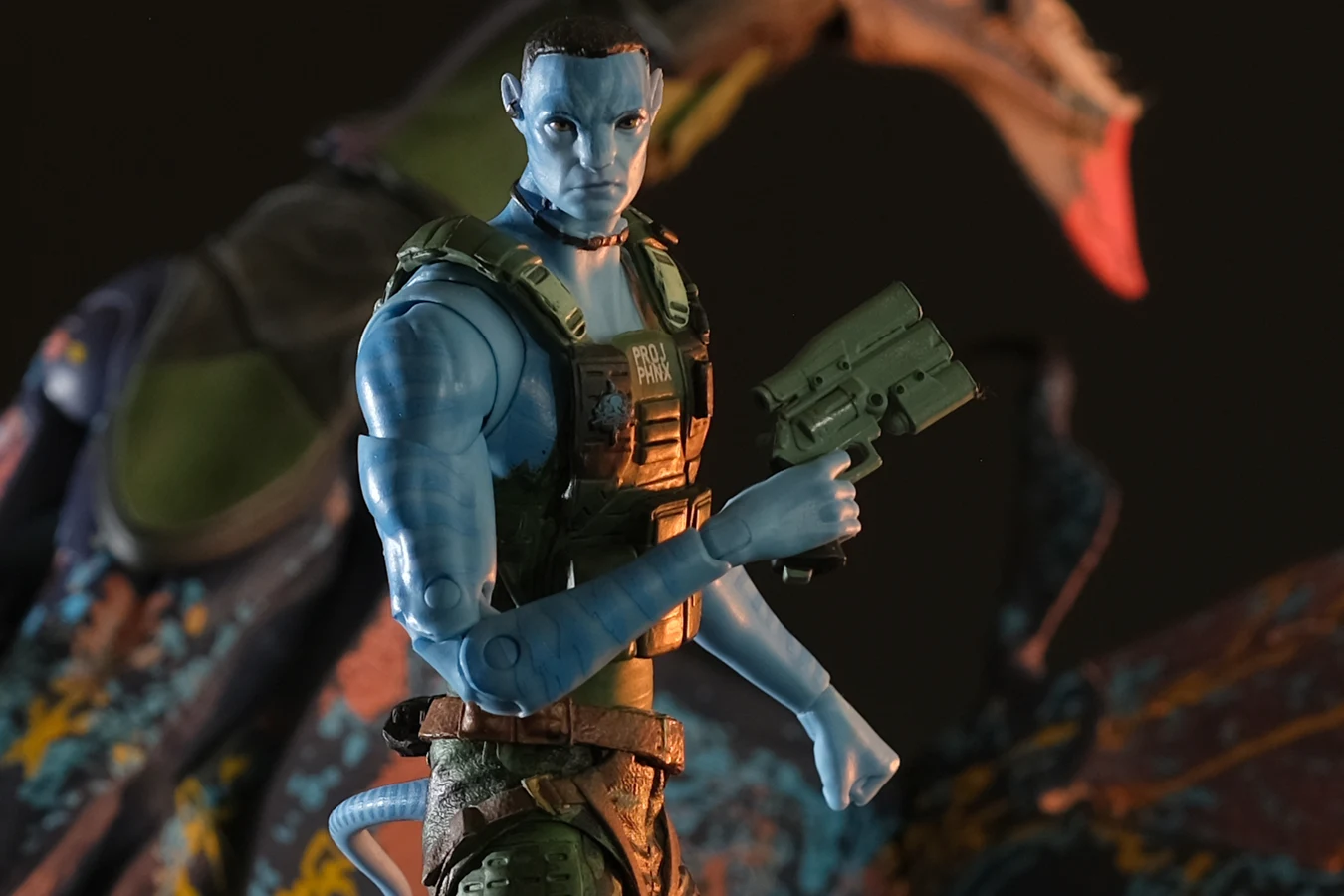 McFarlane 7-inch Recom Quaritch action figure with Project Phoenix vest, pistol, and RDA Banshee in the background