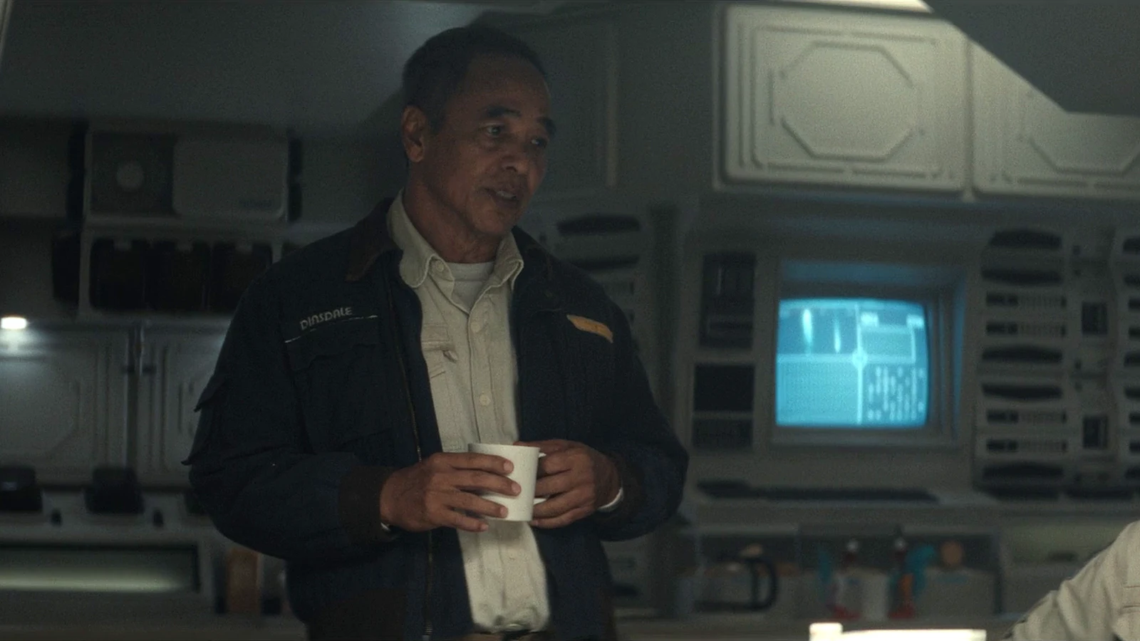 Captain RJ Dinsdale holding a mug in his Maginot jacket in the mess hall in Alien: Earth