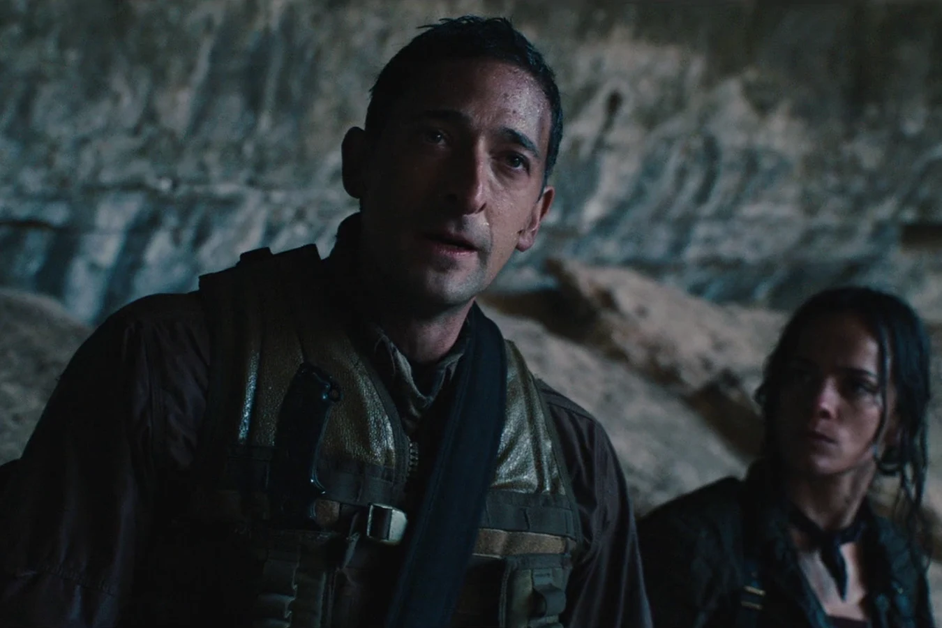 Royce speaking in front of a grey rock wall with Isabelle standing behind him