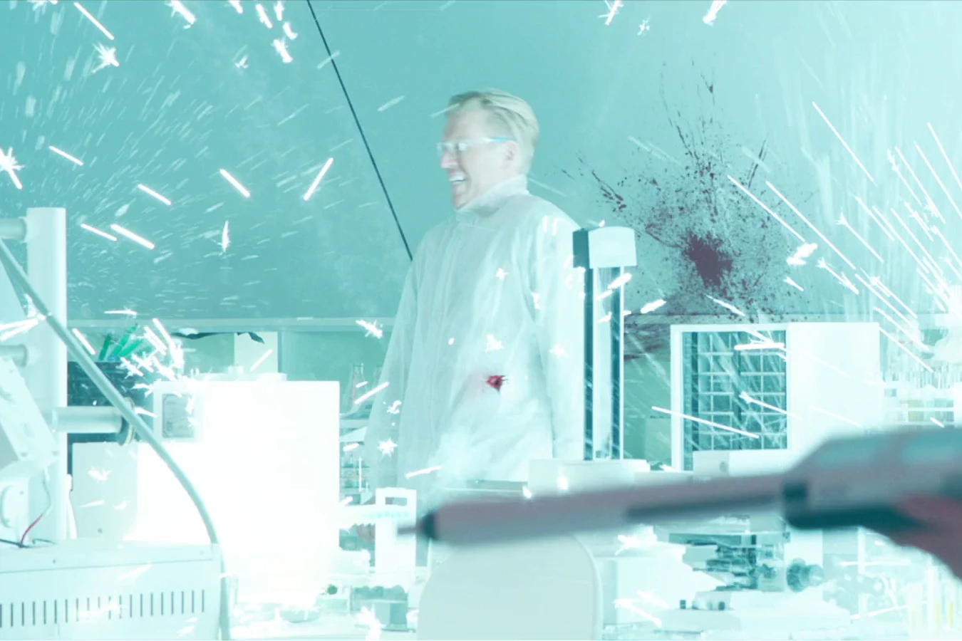Sean Keyes, bloodied, in a lab full of flying sparks and a blood splatter on the wall, as Casey Brackett aims a weapon in the foreground