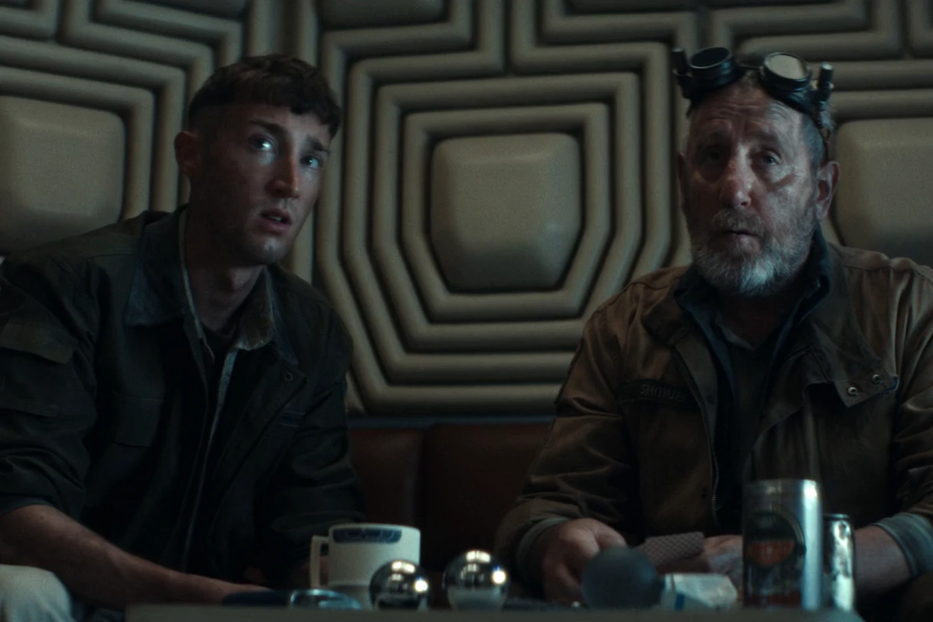 Shmuel in goggles seated beside a younger crewmate in the Maginot lounge in Alien: Earth Neverland