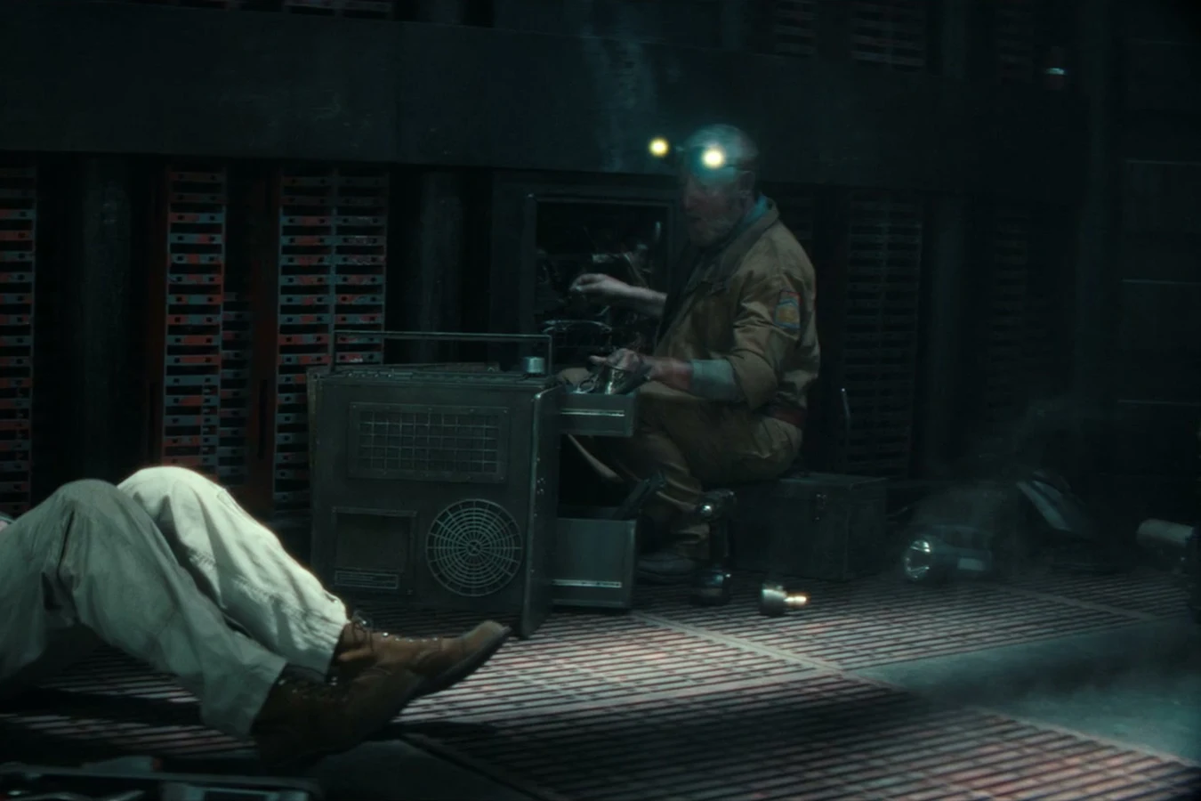 Shmuel working at an open Maginot panel with headlamps while Malachite waits nearby in Alien: Earth