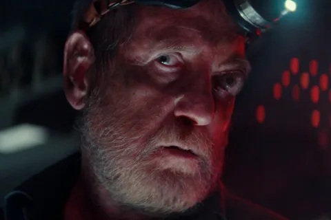 Close-up of Shmuel lit in red with a headlamp on his brow aboard the Maginot in Alien: Earth