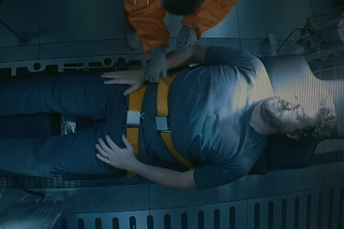 A technician in orange strapping Tennessee into a test chair, seen from above