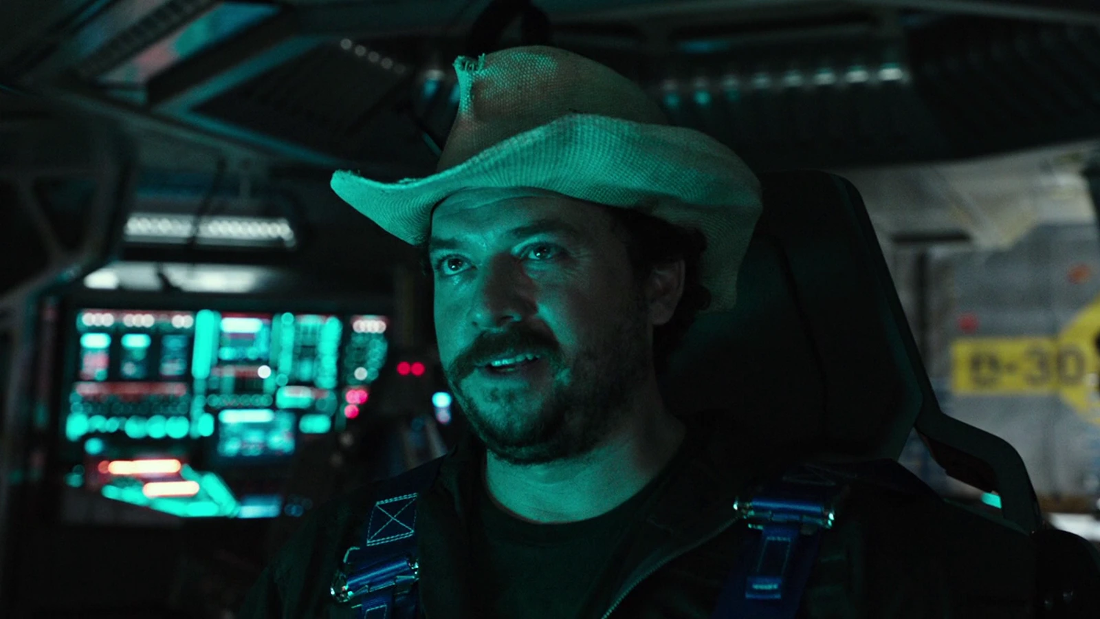 Tennessee in his cowboy hat and flight harness at the controls, teal console light on his face
