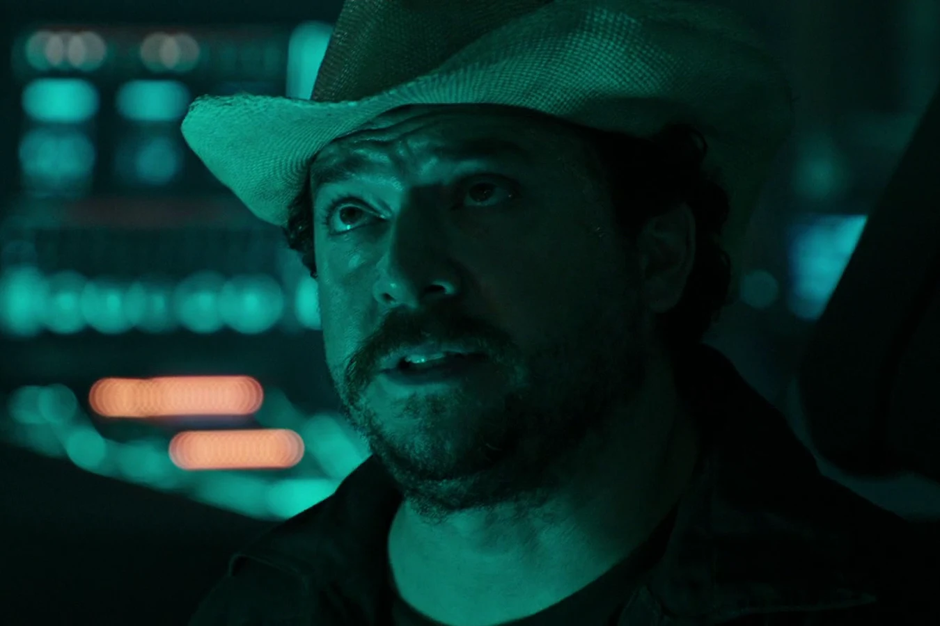 Close-up of Tennessee in his cowboy hat, speaking in the dim cockpit