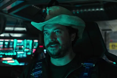 Tennessee in his cowboy hat and flight harness at the controls, teal console light on his face
