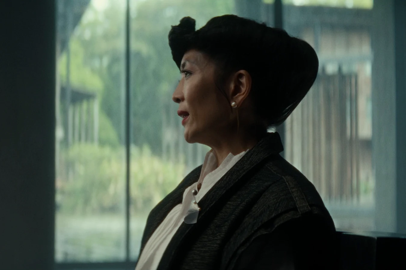 Yutani in a black hat and jacket seated by the windows of the arbitration room in Alien: Earth