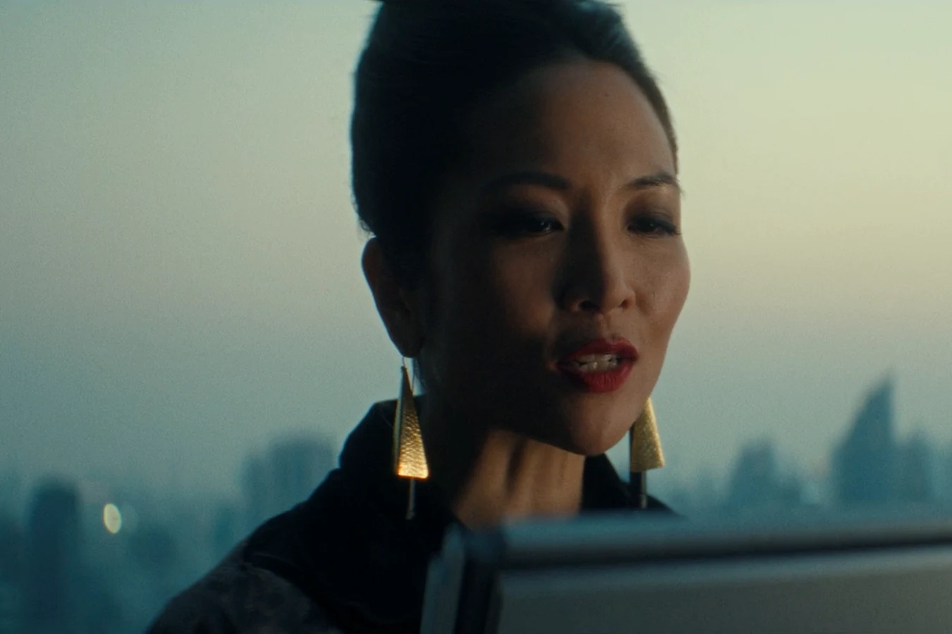 Yutani speaking on a video call in front of a misty city skyline in Alien: Earth